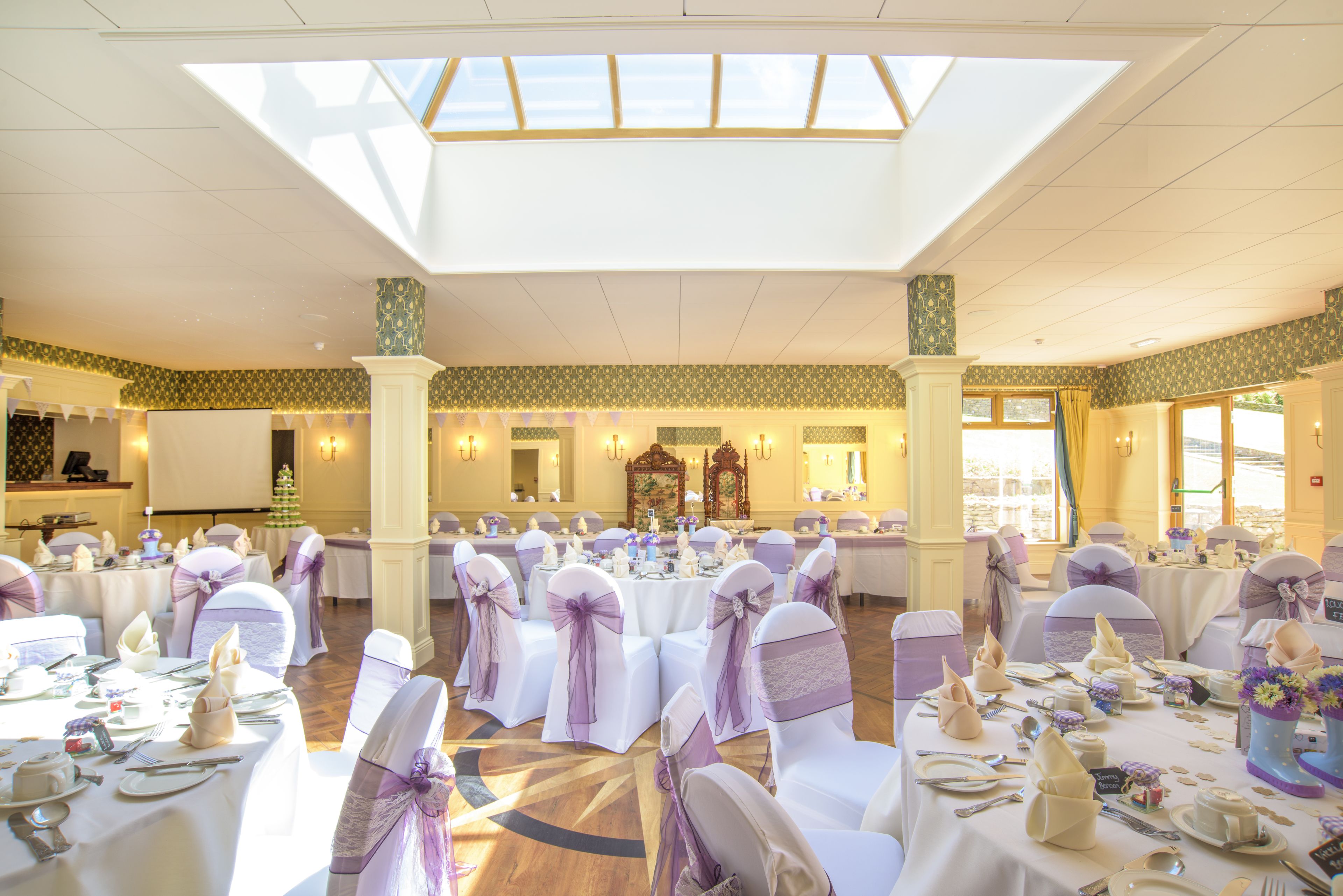 A banquet hall with round tables, white tablecloths, and purple sashes on chairs.