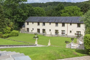 Un grand bâtiment blanc, surmonté d’un toit gris, entouré de pelouses bien entretenues et de chemins pavés de pierres.