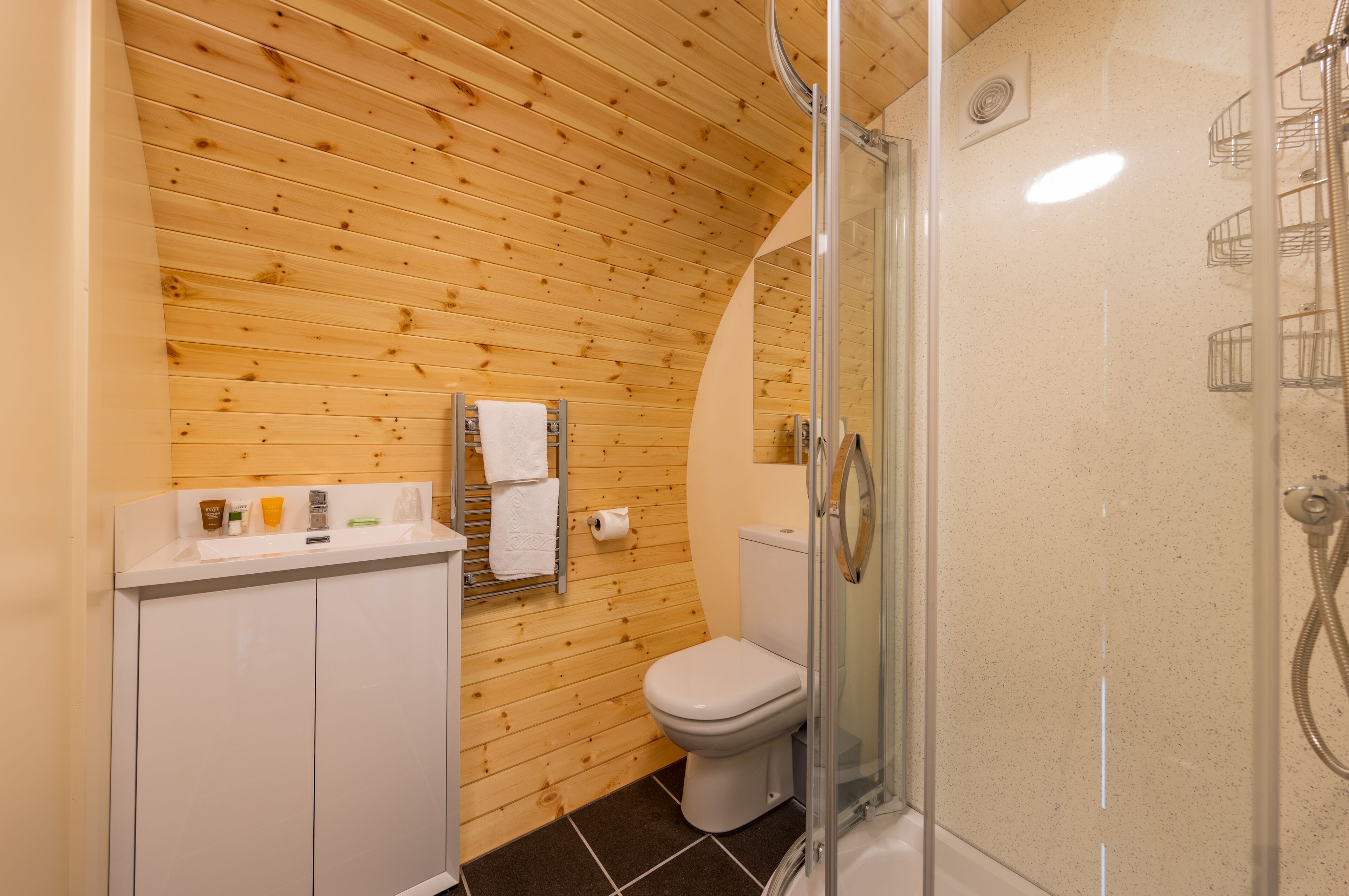 A bathroom with wooden panel walls, a white sink, a toilet, and a glass-enclosed shower area.