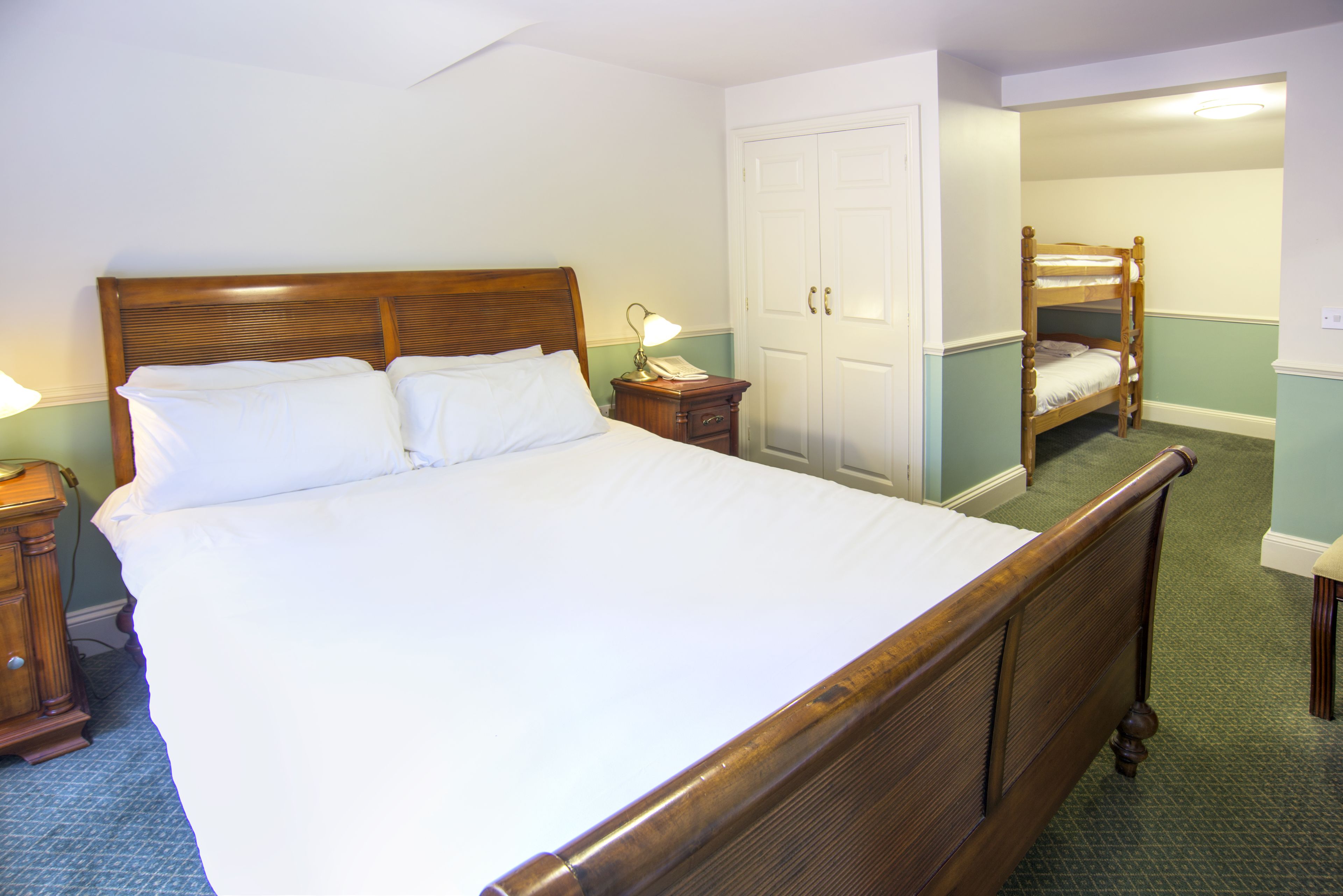 Un dormitorio con una cama de madera grande, una mesita de noche con lámpara, un armario y un espejo.