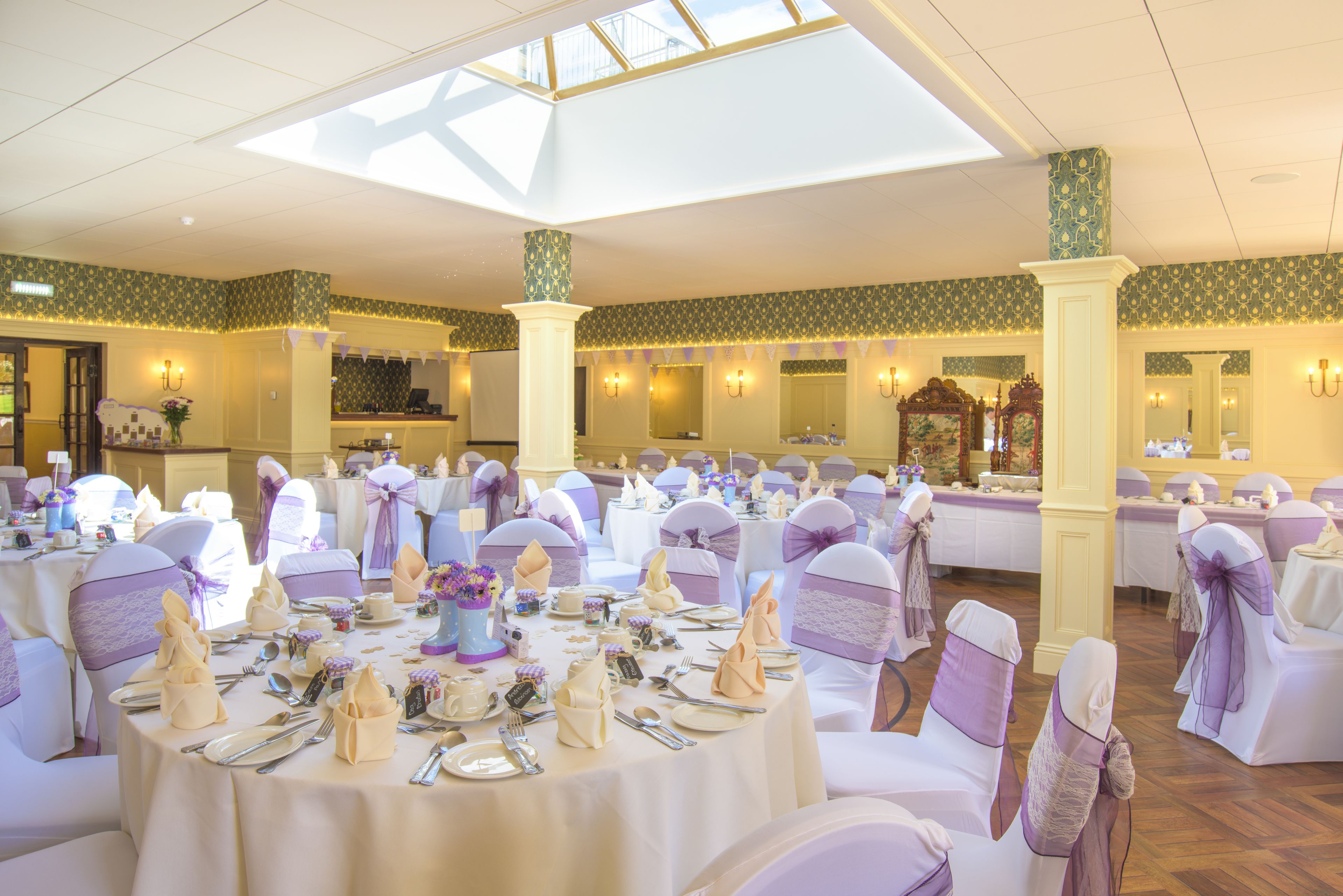 A banquet hall with round tables set for a formal event, featuring white tablecloths and purple sashes on chairs.