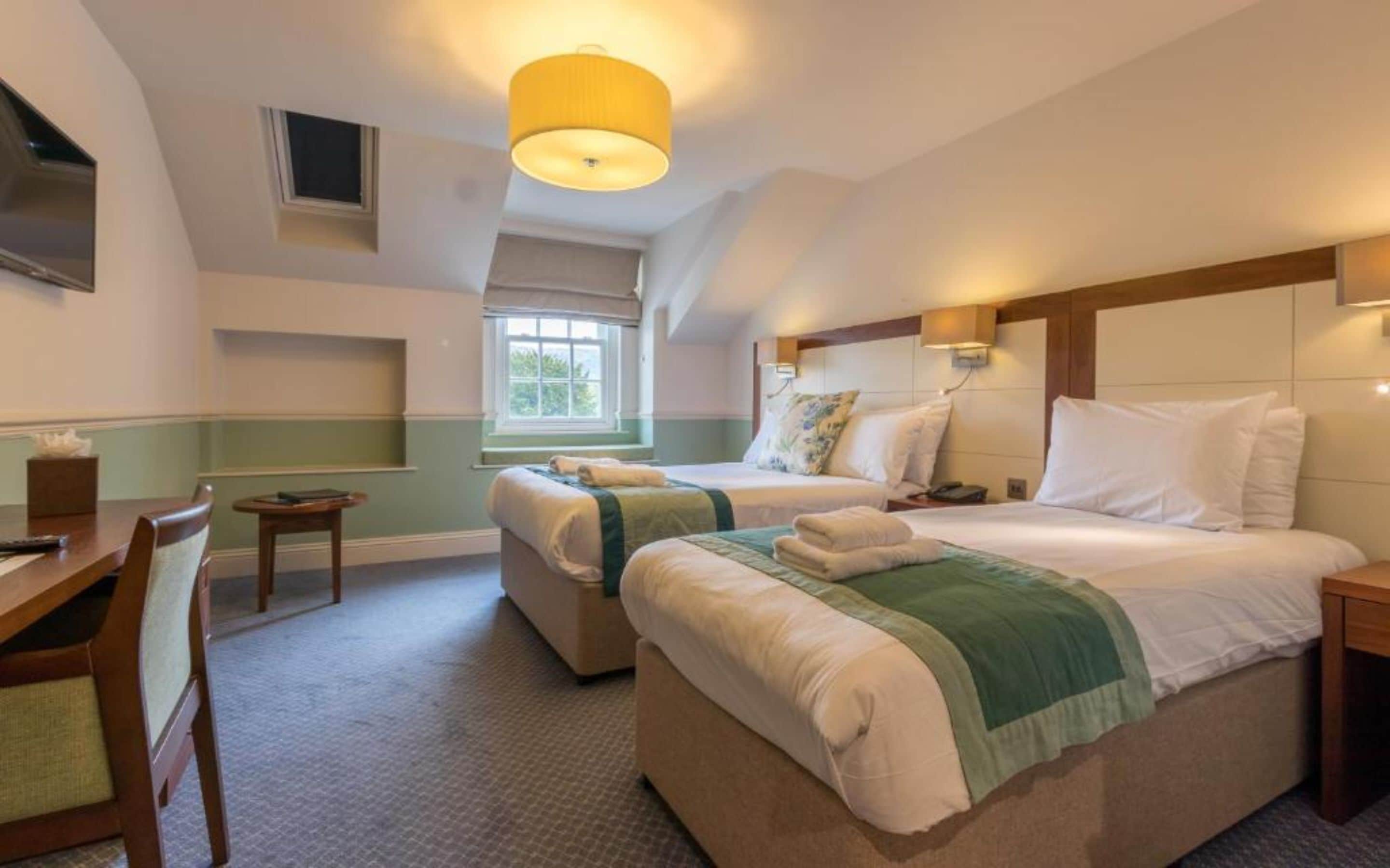 A hotel room with a large bed, a desk, a chair, and a window with blinds.