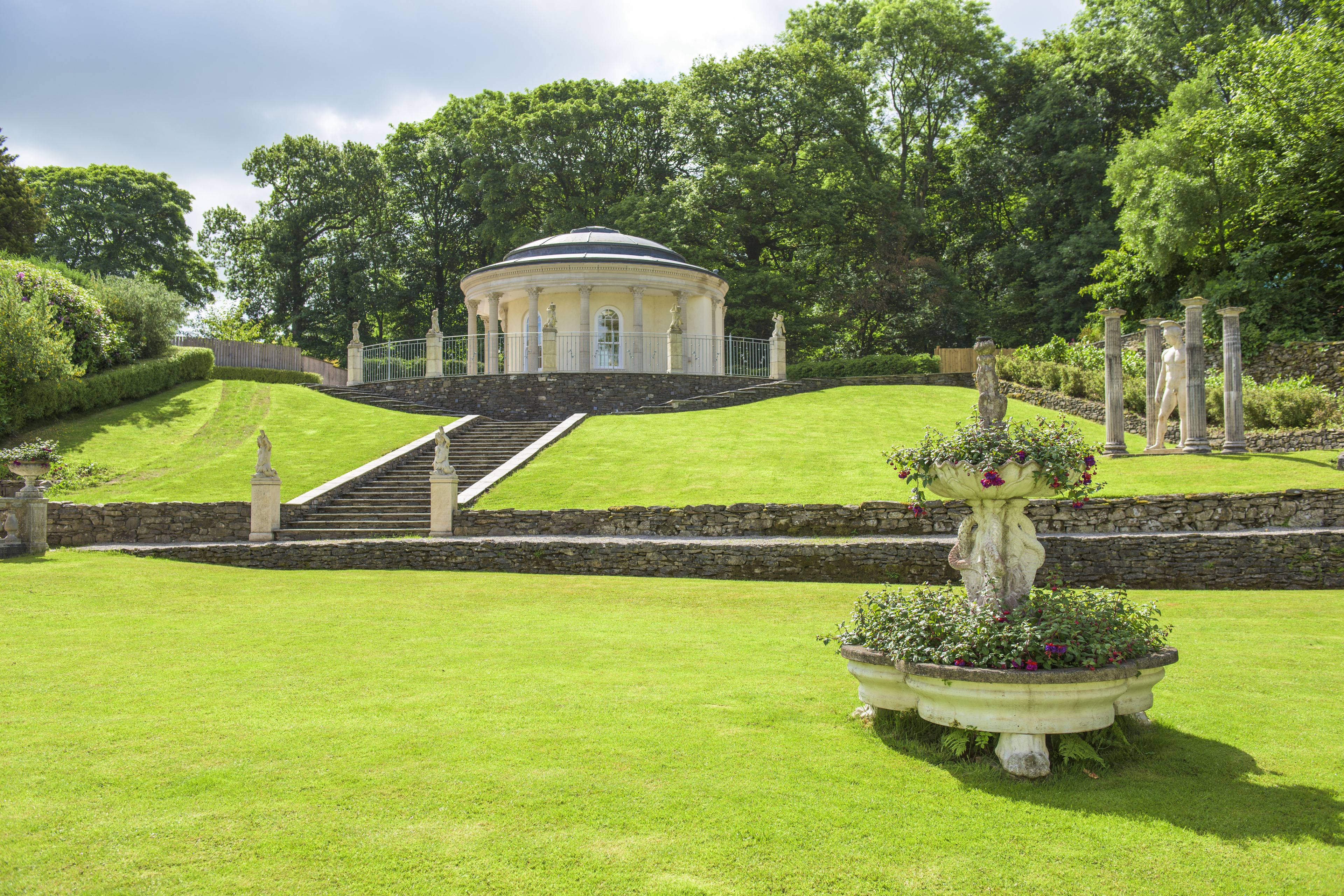 A landscaped garden with a central gazebo, stone steps, and a fountain.