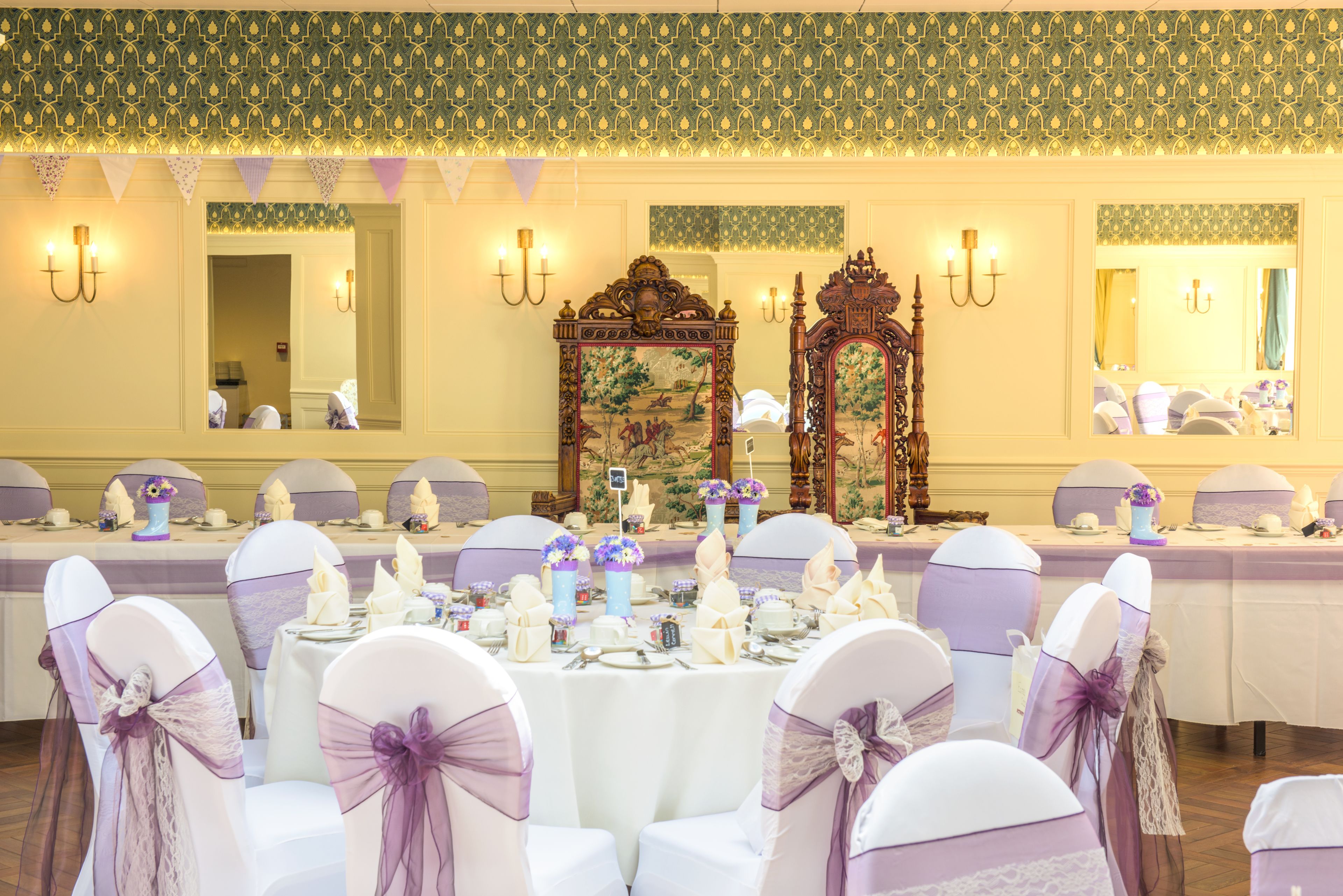 A banquet hall with round tables set for a formal event, adorned with white tablecloths and purple sashes.