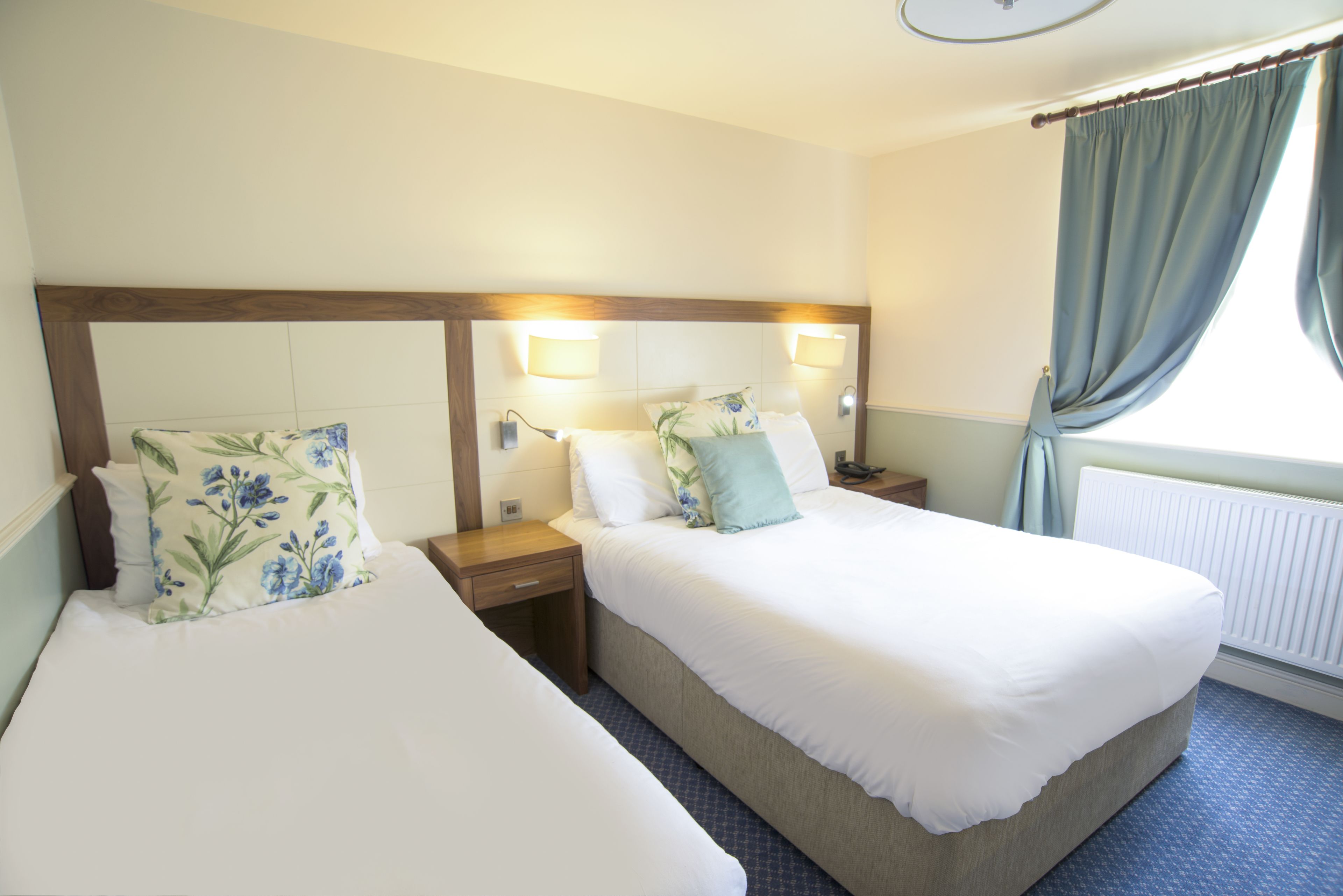 A hotel room with two single beds, a wooden headboard, bedside lamps, and a window with curtains.