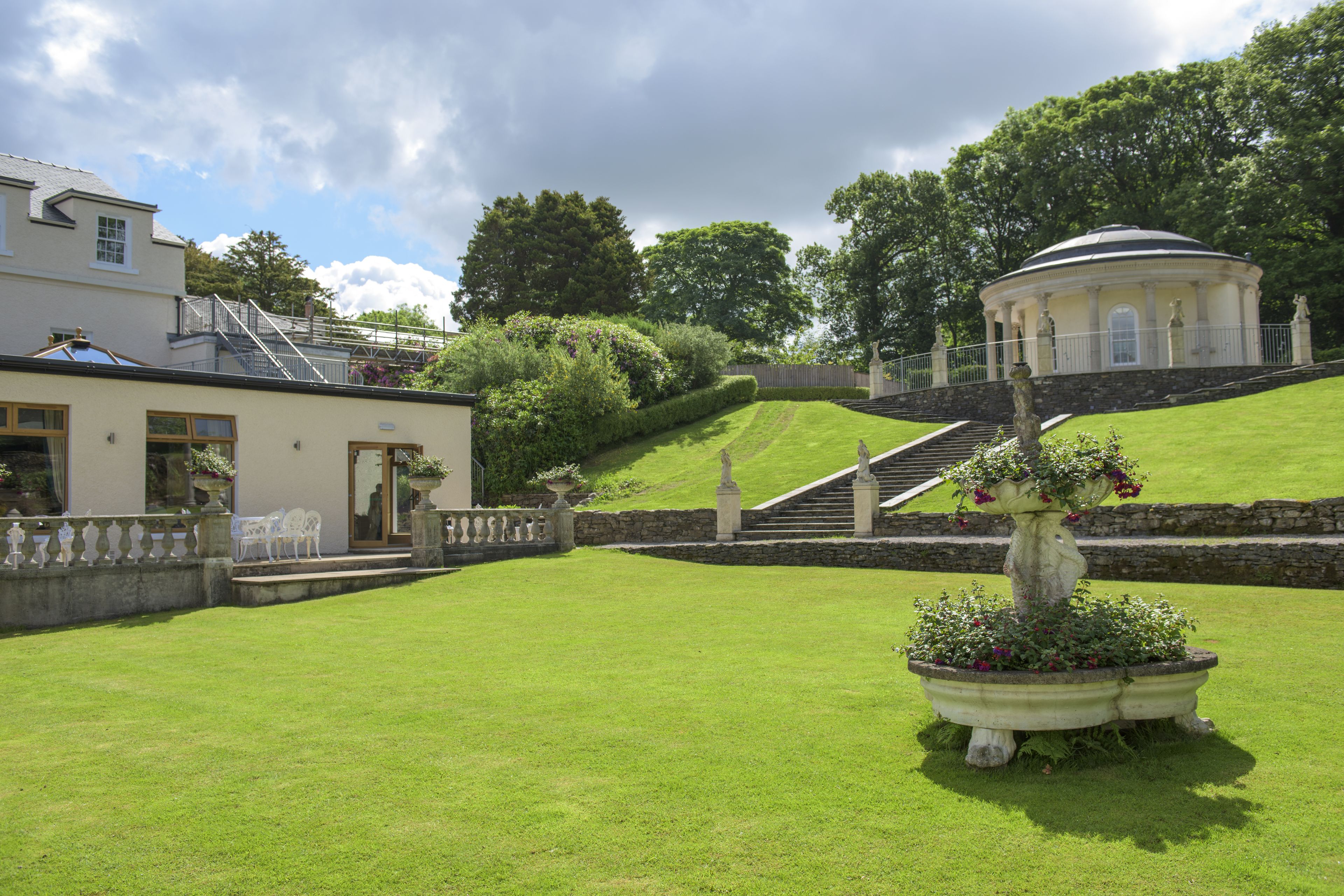 A well-maintained lawn with a stone staircase leading to a building, surrounded by lush greenery and a clear sky.