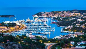 A marina with numerous boats docked, surrounded by residential buildings and a hilly landscape. - CPH - Pevero Hotel (Arzachena)