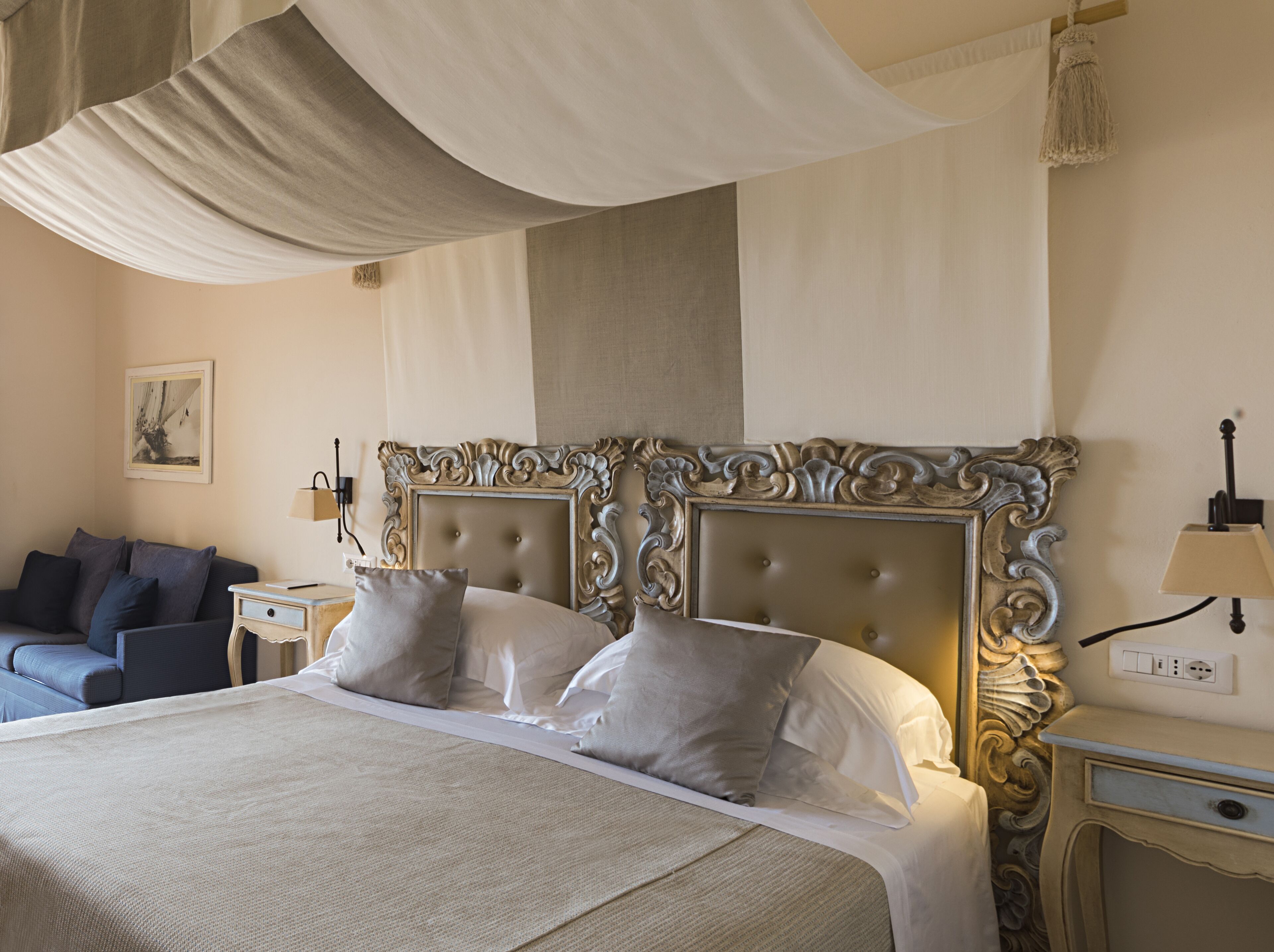 Un lit bien fait, doté d’une tête de lit capitonnée, une table de chevet avec une lampe et un canapé dans une chambre d’hôtel.