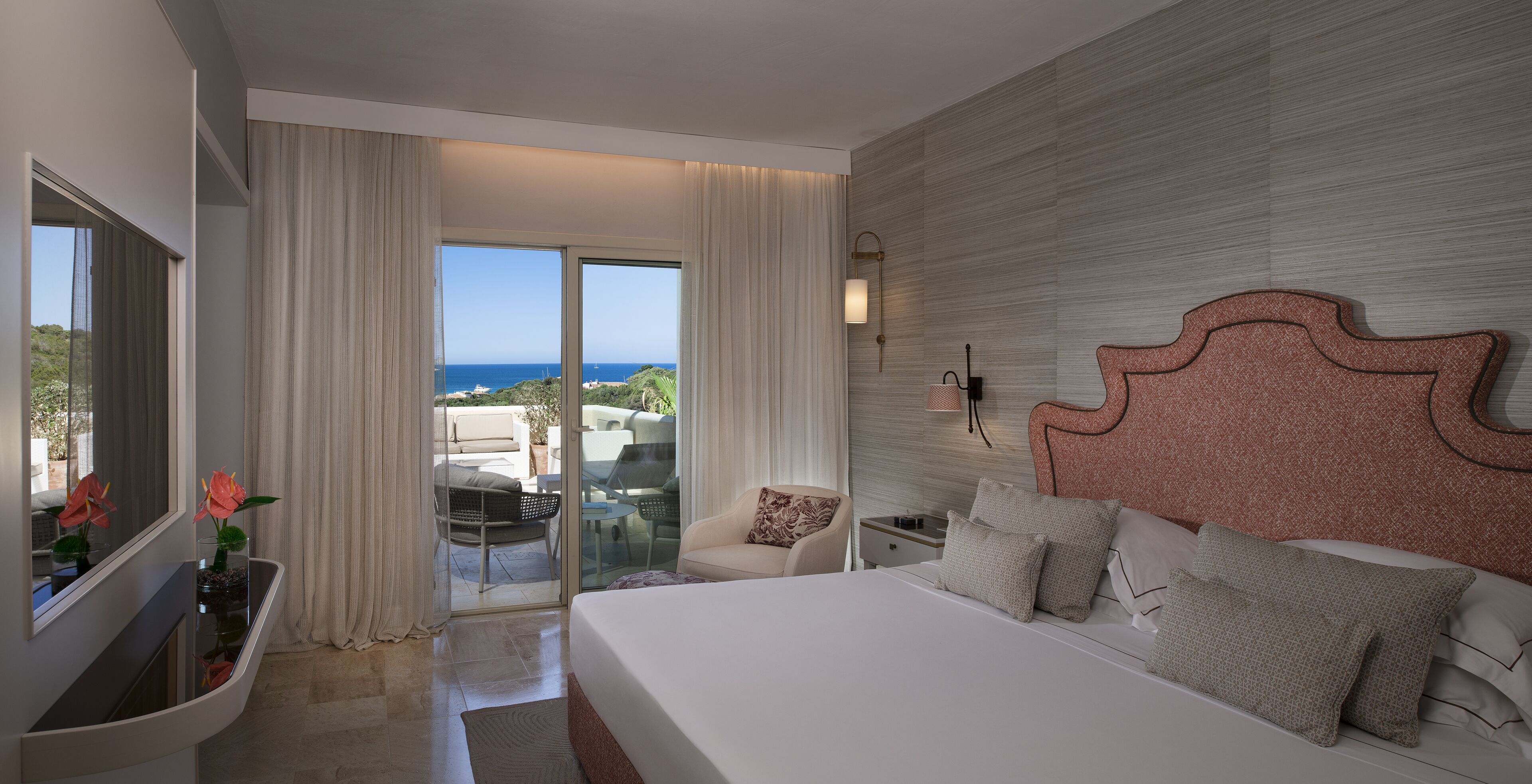 Una camera d'albergo moderna con un letto grande, un comodino, una scrivania e vista sull'oceano tramite una porta scorrevole in vetro.
