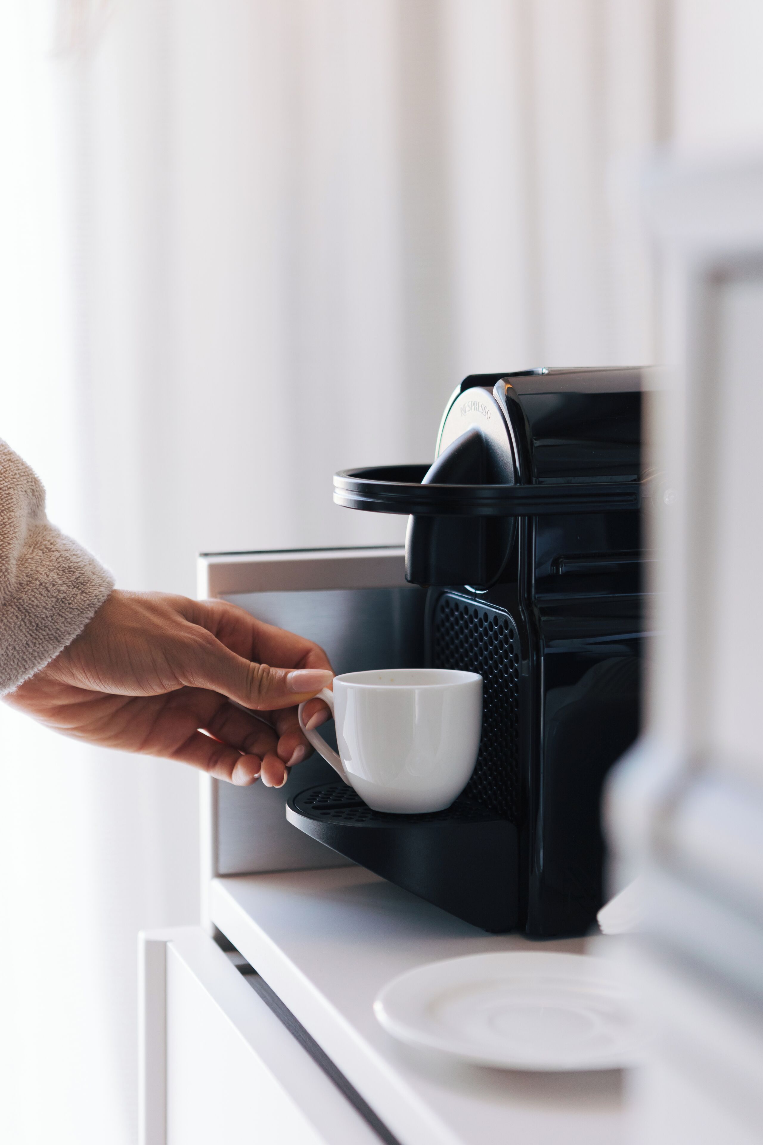 A hand holding a white cup near a black coffee machine.