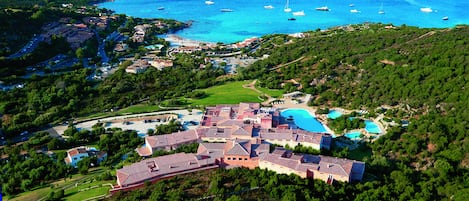 An aerial view of a coastal resort with multiple swimming pools, a large central building, and a marina with boats.