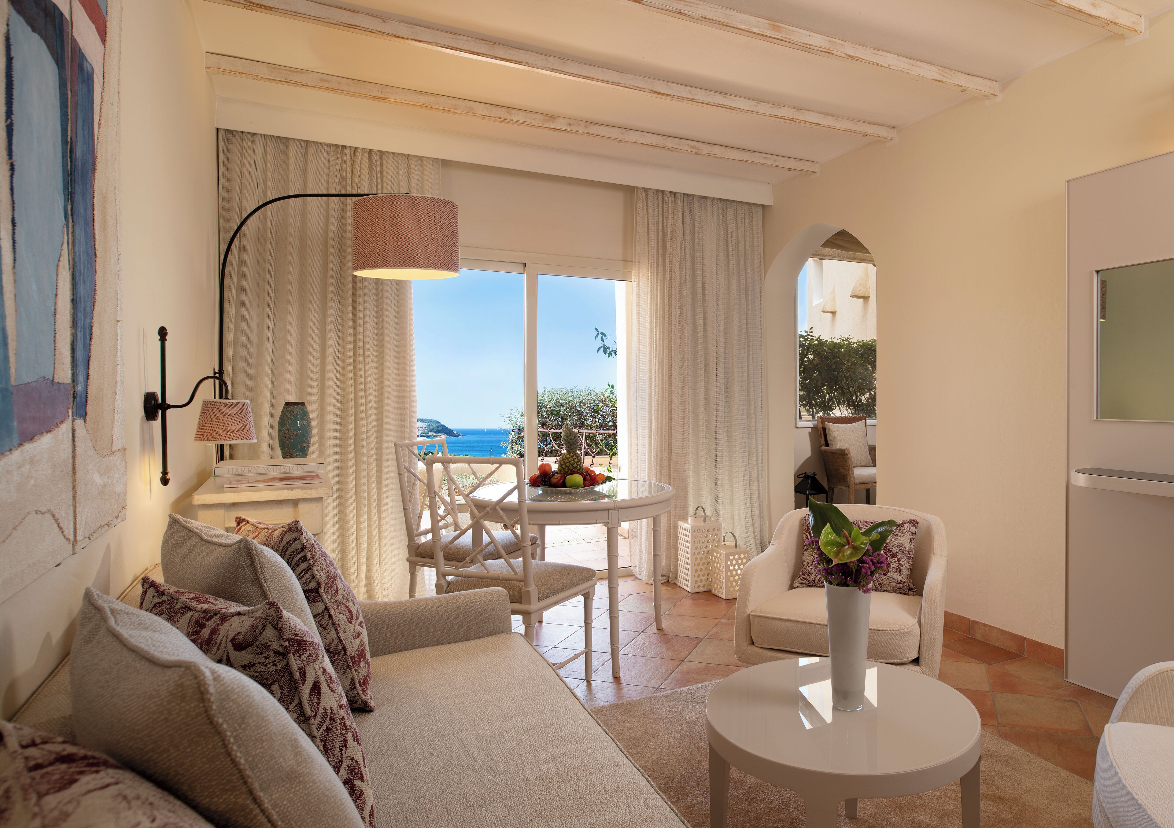 A modern living room with a sofa, a round table, and a view of the sea through large windows.