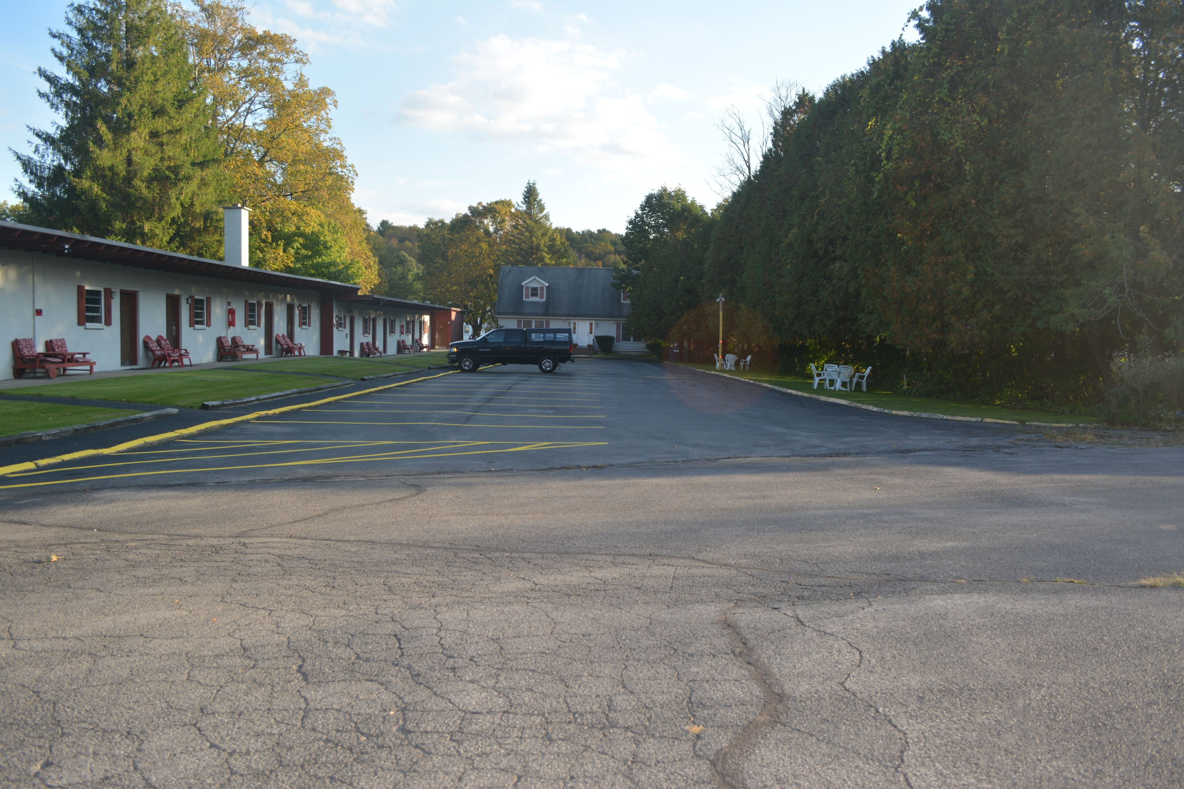 A motel with a row of rooms, a parking lot, and a large tree in the background.