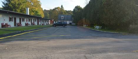 A motel with a row of rooms, a parking lot, and a large tree in the background.