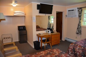 A hotel room with a bed, a desk with a chair, a television mounted on the wall, a small refrigerator, a trash bin, and a heater. - The Village Motel (Richfield Springs)
