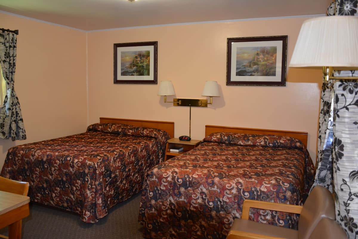 A hotel room with two beds, a nightstand, a lamp, and two framed pictures on the wall.