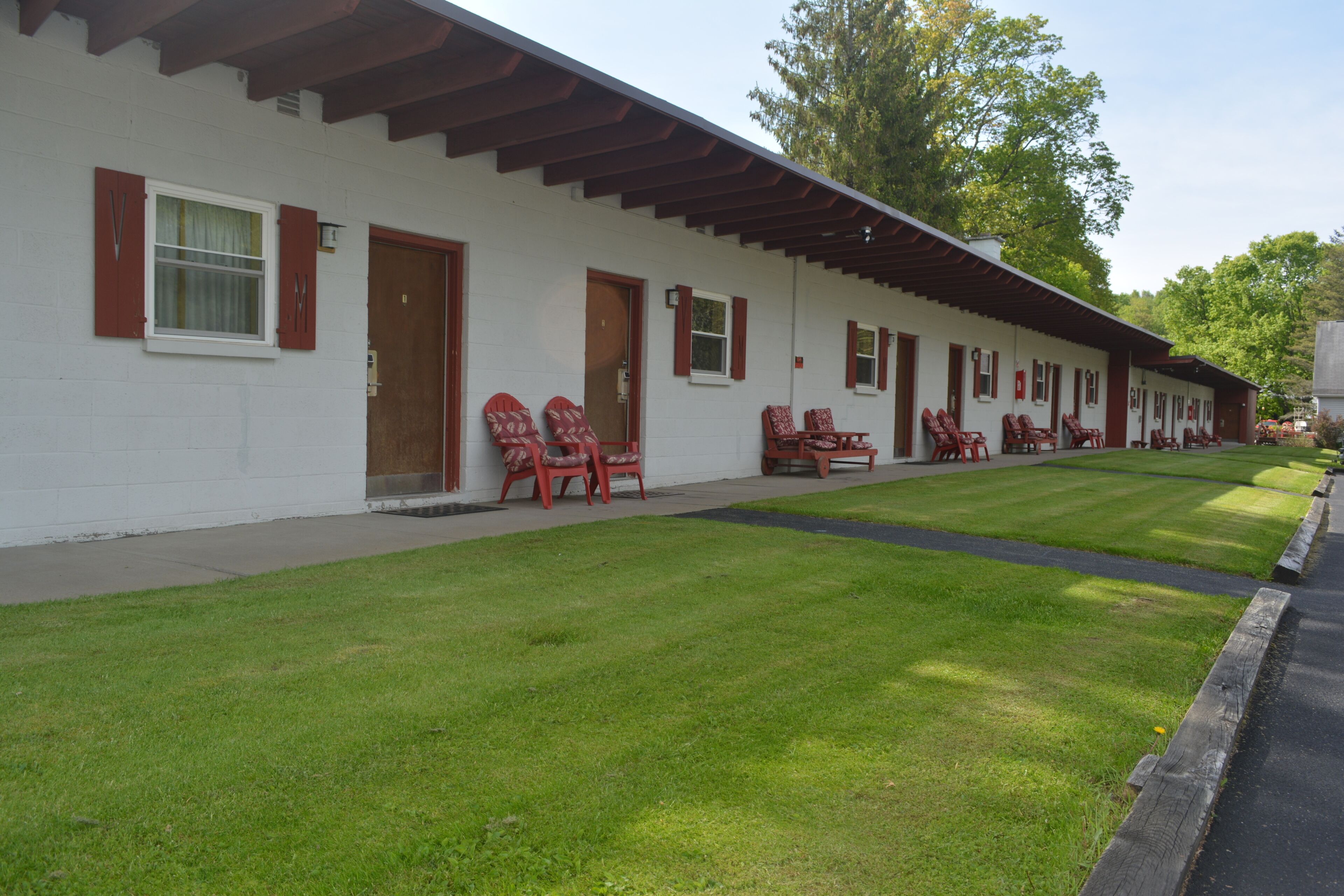Een wit gebouw met rode luiken en een overdekte veranda met rode stoelen.