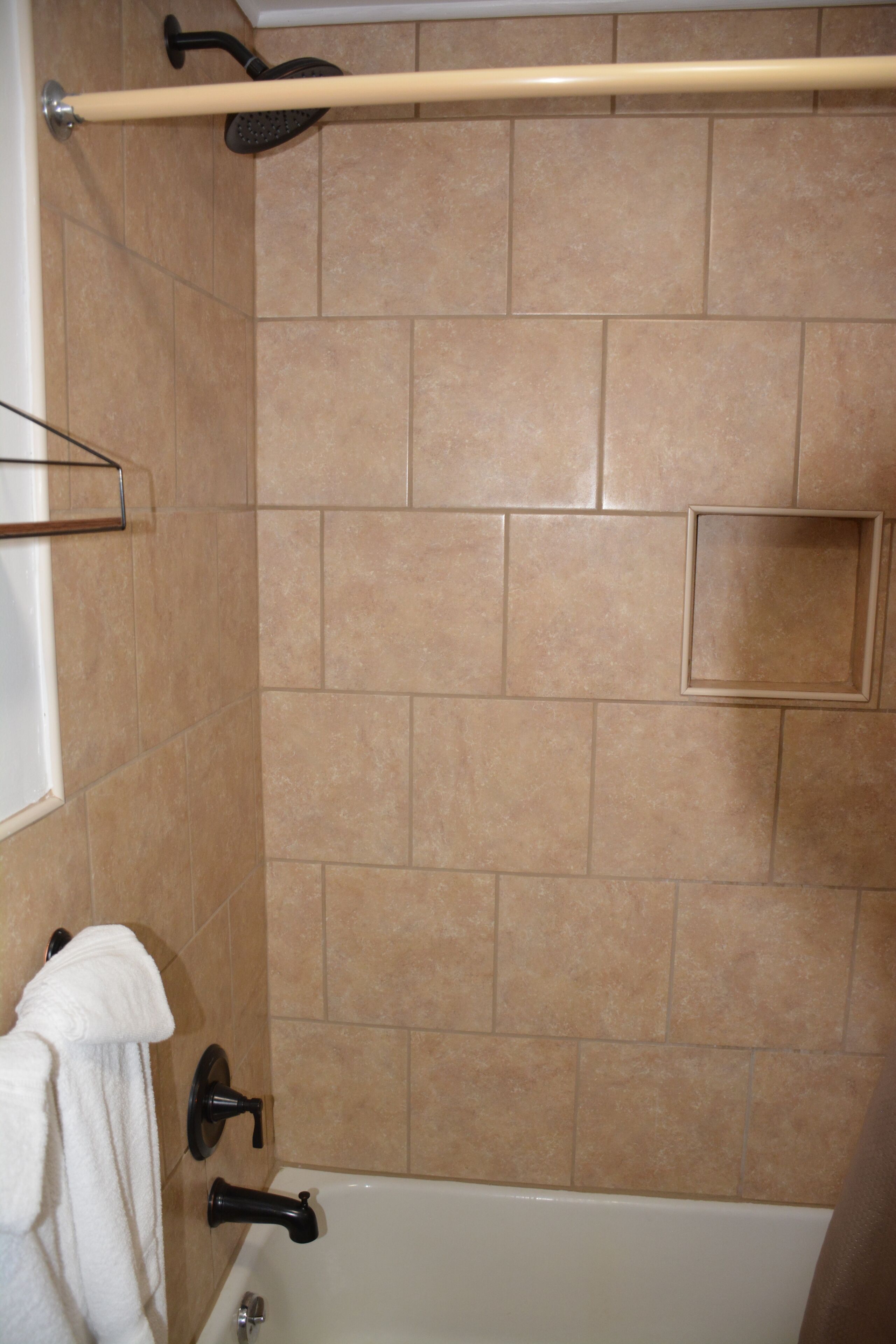 A bathroom with beige tiles, a white bathtub, a towel rack, and a showerhead.