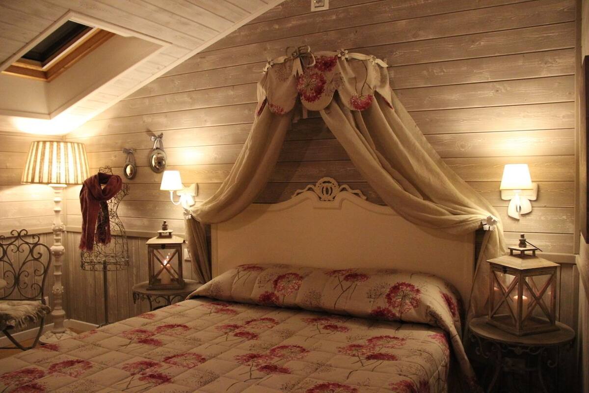 Un dormitorio con cama a dosel, dos mesitas de noche con lámparas, una lámpara colgante y una pequeña mesa con un farol.