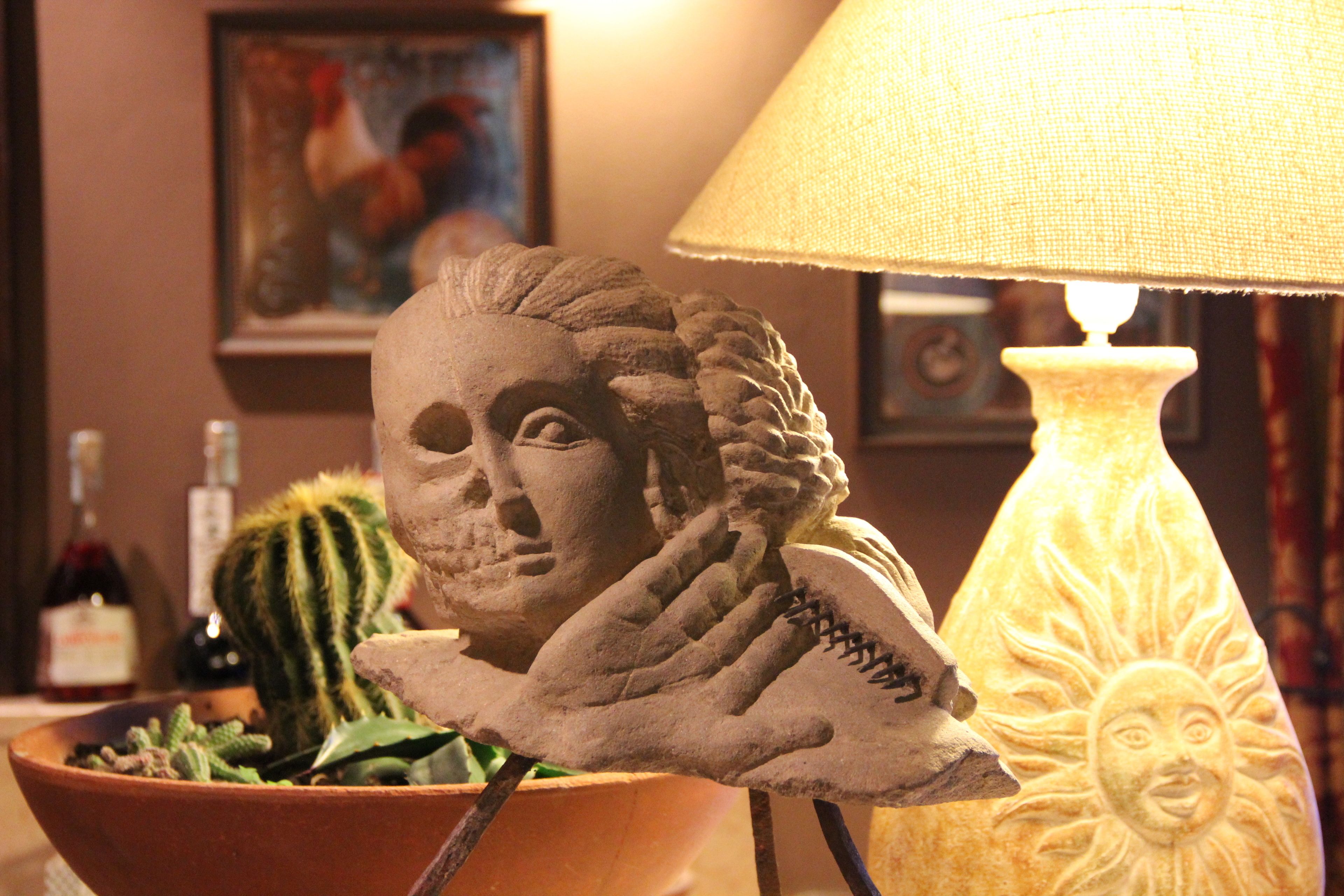 A sculpture of a human face with a cactus and a sun, placed on a table next to a lamp.