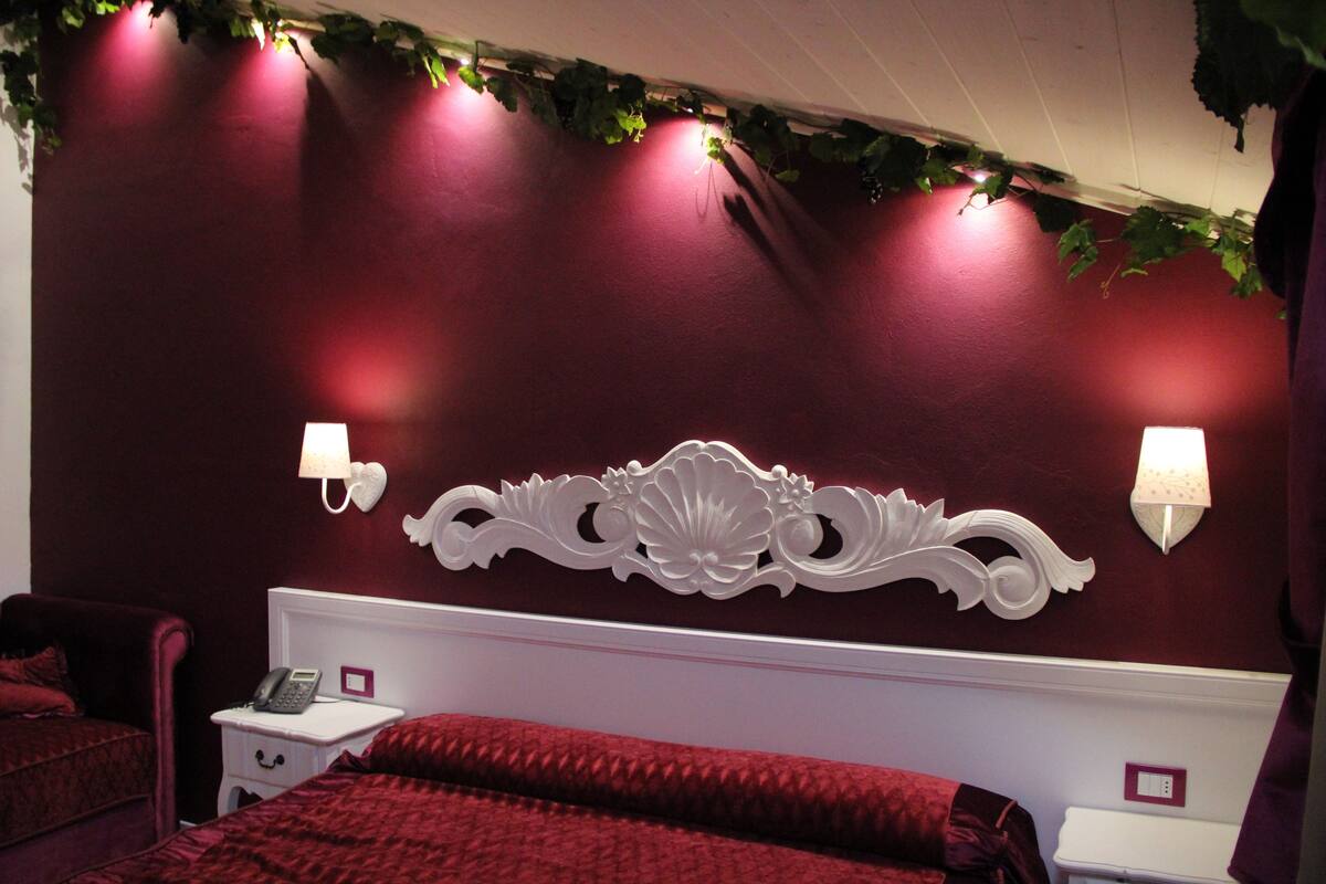 Una habitación de hotel con una pared roja, un cabecero blanco y dos lámparas de noche.