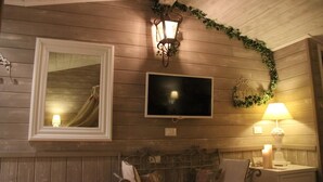 Ein Zimmer mit Holzwandverkleidung, einem wandmontierten Flachbildfernseher, einer Wandleuchte und einem Nachttisch mit Lampe und Kerze.