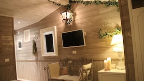 Ein gemütlicher Raum mit einer Holzwand, einer Bank, einem kleinen Tisch mit Kerzen und einem an der Wand befestigten Fernseher.