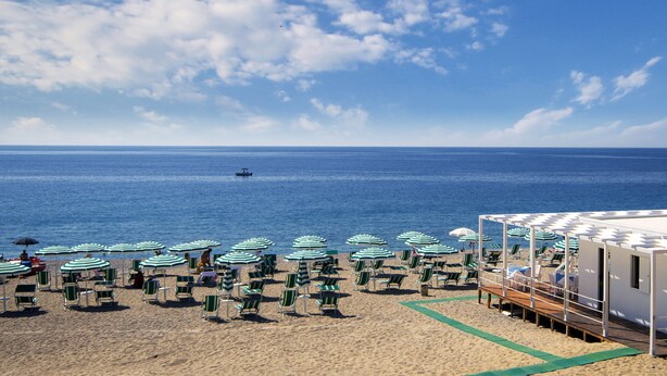 A beach with rows of green and white striped umbrellas and chairs, a lifeguard station, and the ocean in the background. - Hotel Rada Siri (Montepaone Lido)