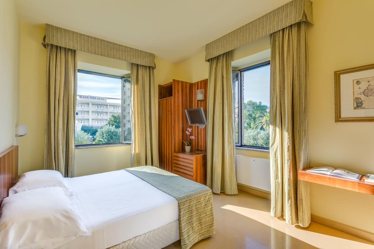 A hotel room with a bed, a wooden dresser, a TV, and a window with curtains.