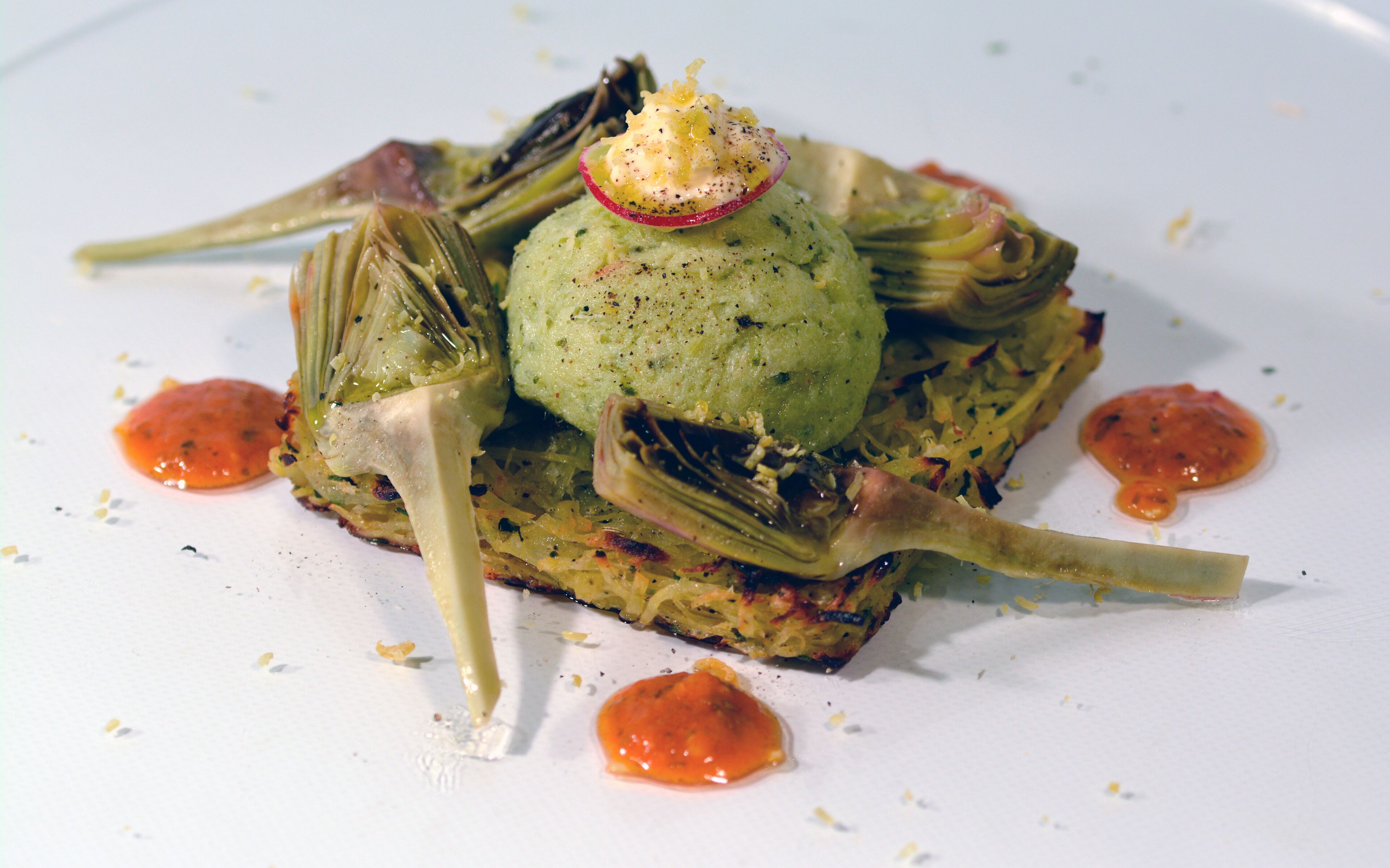A dish with artichoke hearts, green puree, and sauce on a white plate.