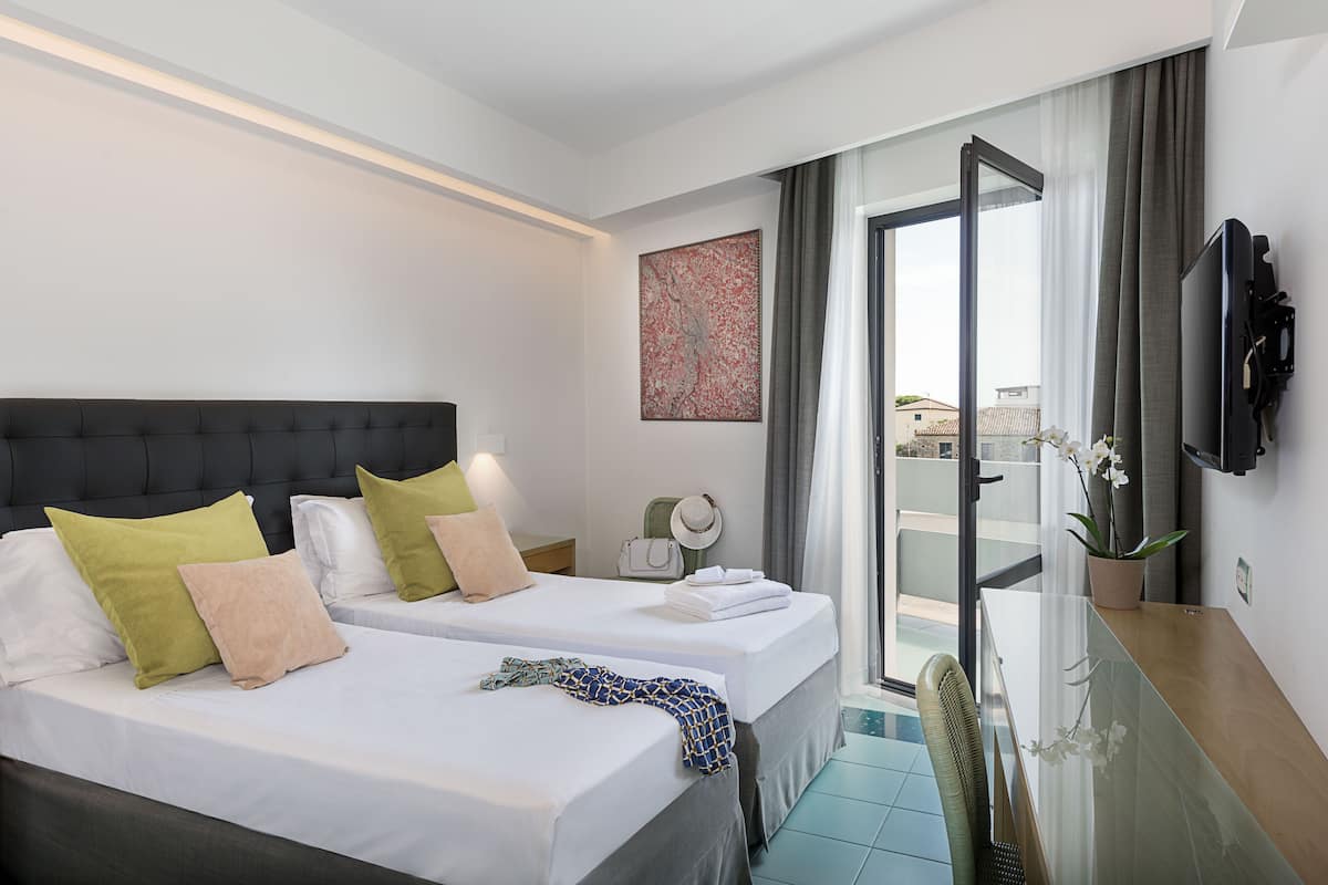 A hotel room with two beds, a television, a desk, and a view of the outside.