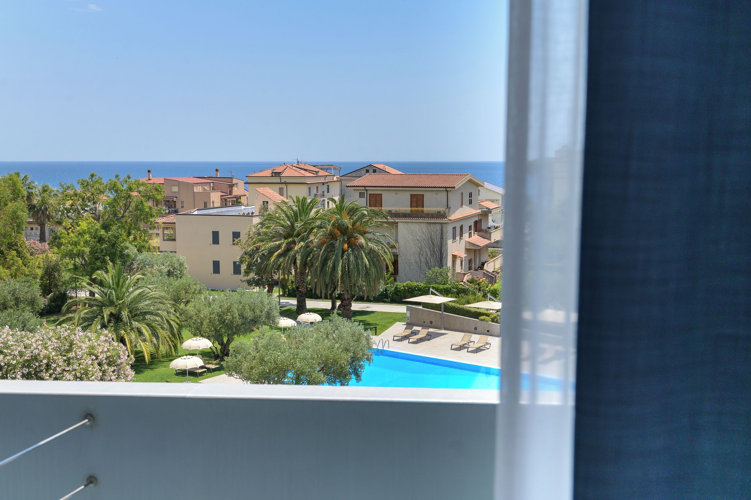 A view of a residential area with a swimming pool, palm trees, and buildings with red roofs.