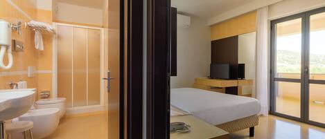 A modern hotel room with a bathroom, a bed, a TV, and a balcony with a view.