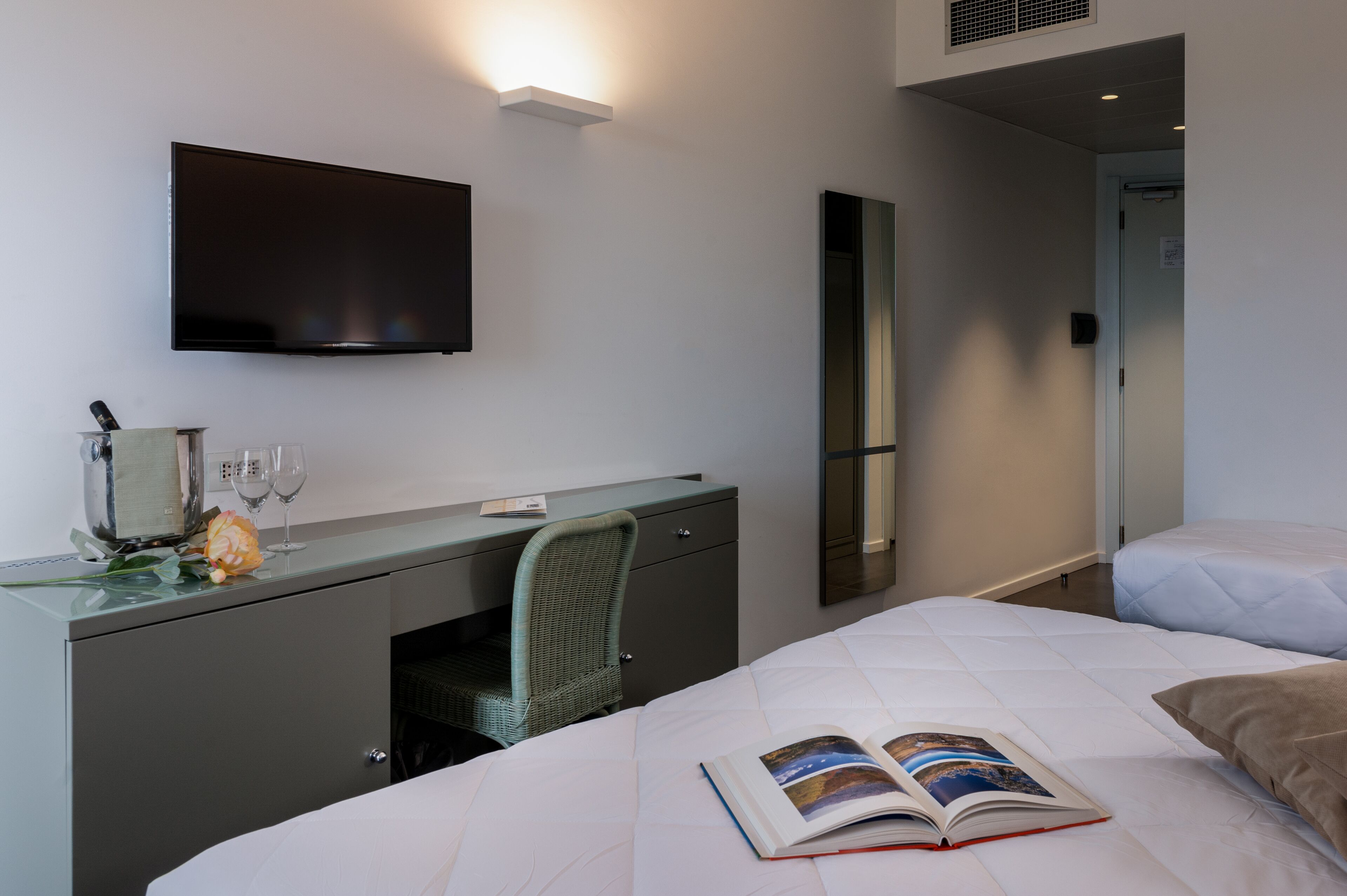 A hotel room with a bed, a desk with a chair, a flat-screen TV, and a mirror.