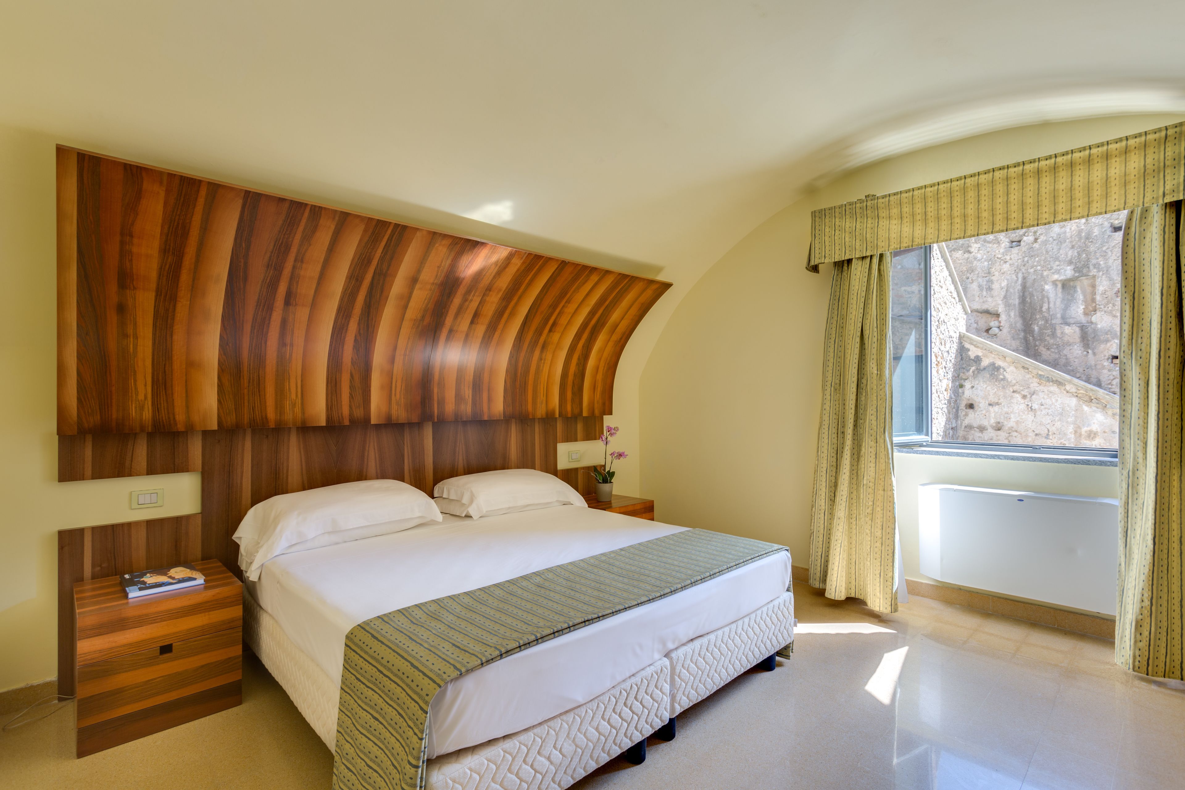 Un dormitorio con una cama grande, cabecera de madera, mesitas de noche y una ventana con cortinas.