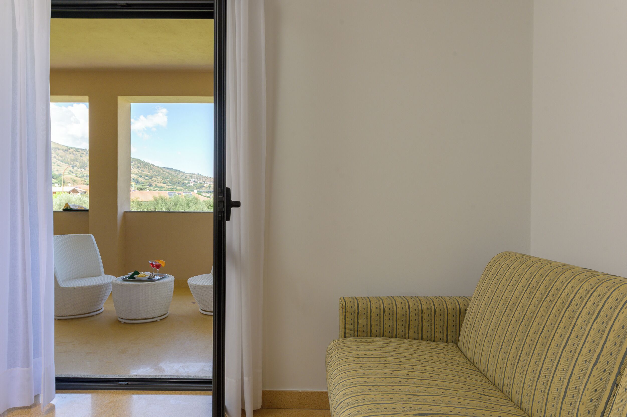 Una habitación con sofá, una silla, una mesita con fruta y vistas a un paisaje a través de una puerta.