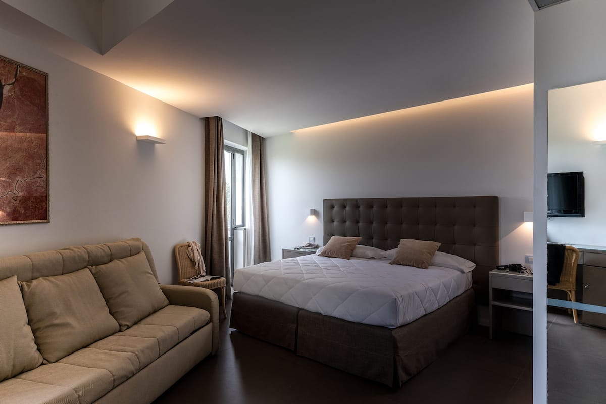 A modern hotel room with a large bed, a sofa, a desk, and a TV.