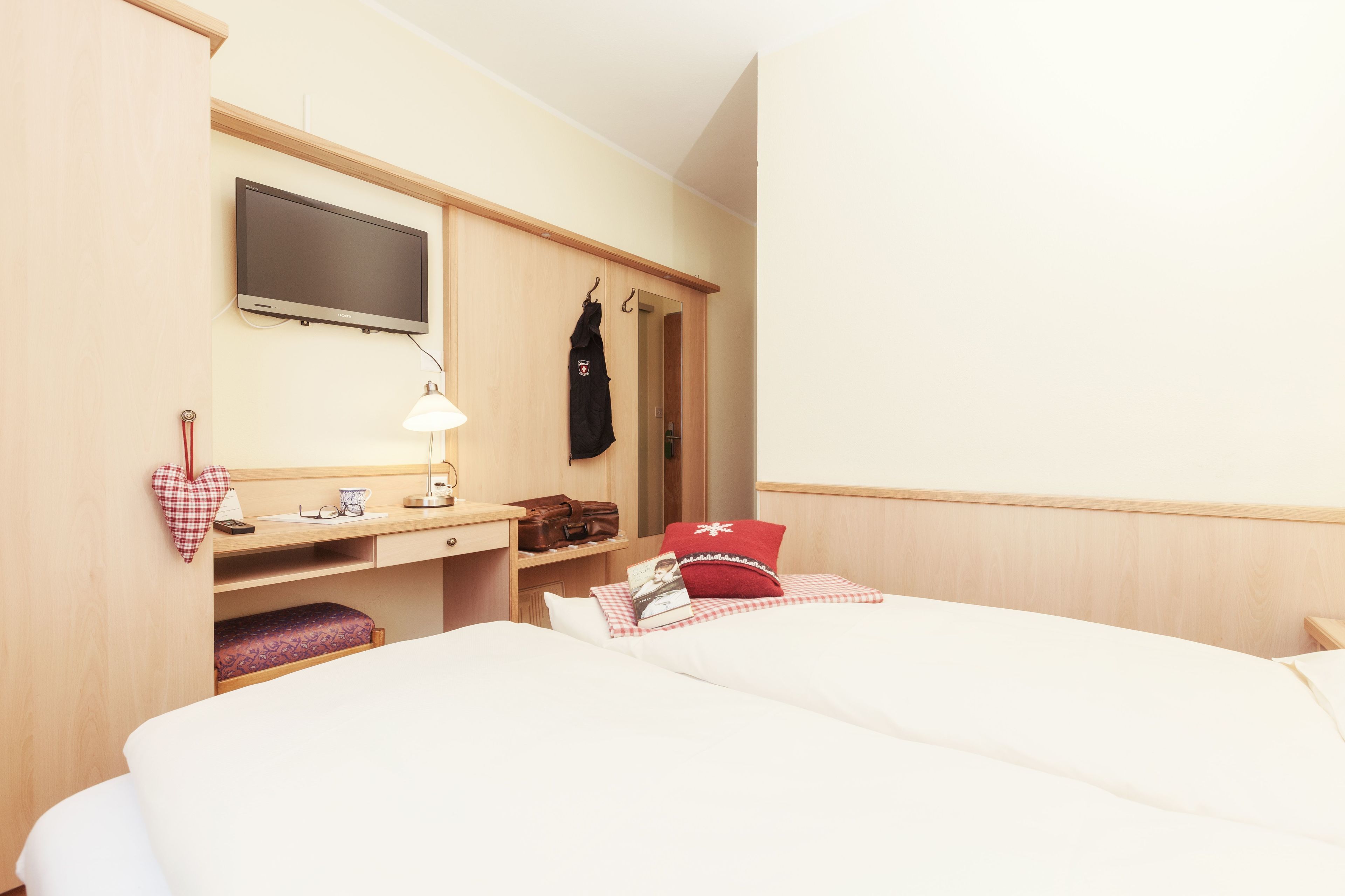 Una habitación de hotel con dos camas, un escritorio con lámpara, un televisor y un armario.