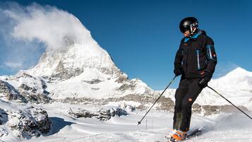 Una persona scia sulle montagne innevate, con terreno roccioso e cielo azzurro limpido.