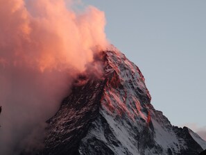 A mountain with a snow-covered peak and a plume of smoke or steam rising from the top. - Le Petit CHARME-INN (Zermatt)