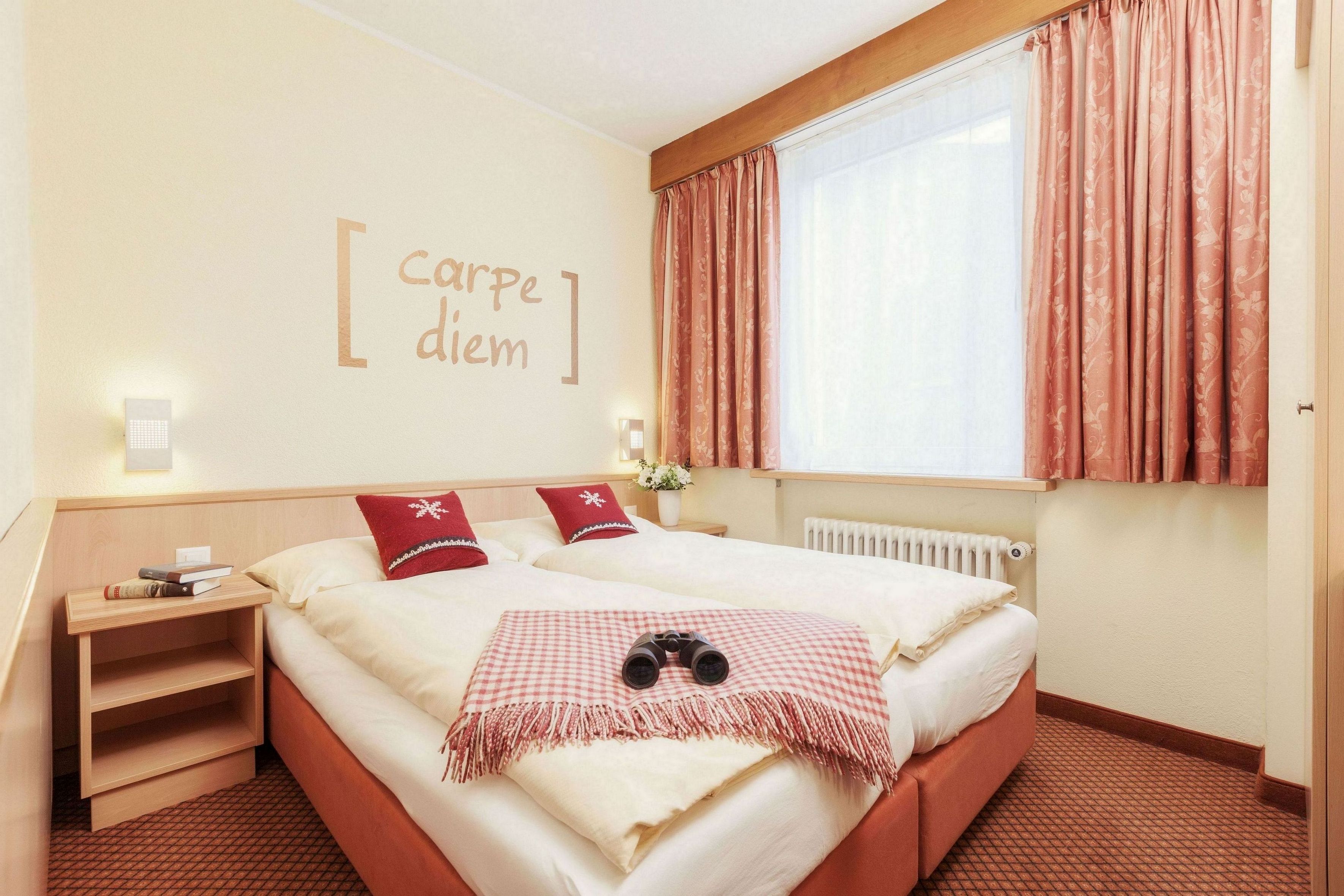 A hotel room with a bed, a nightstand, a window with curtains, and a wall with a sign.