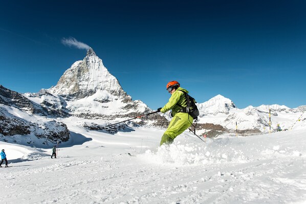 Une personne fait du ski sur une pente enneigée, avec une montagne en arrière-plan.