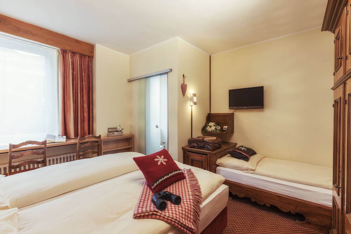 Habitación de hotel con dos camas, un escritorio con silla, un televisor y una puerta decorada con forma de corazón.
