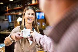 Una persona sosteniendo una taza, probablemente en un bar o cafetería, con estantes al fondo.