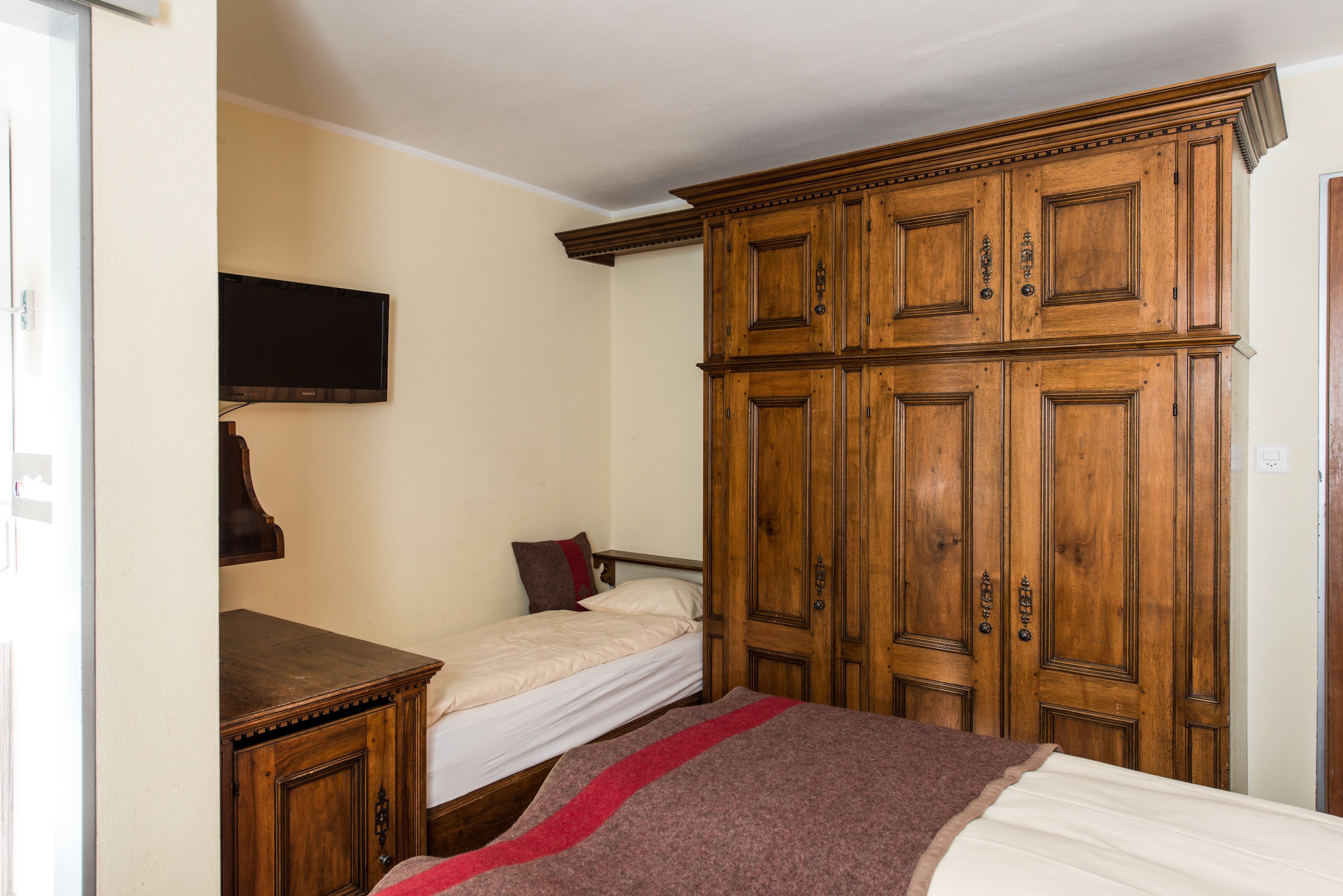 Un dormitorio con una cama individual, un armario de madera y un televisor montado en la pared.