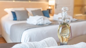 A bottle of perfume on a table in a hotel room with neatly made beds and a nightstand with a lamp. -  La Closerie – SPA & Résidence Hôtel (Deauville)