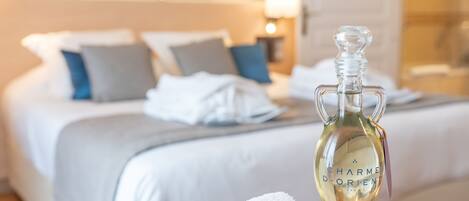 A bottle of perfume on a table in a hotel room with neatly made beds and a nightstand with a lamp.