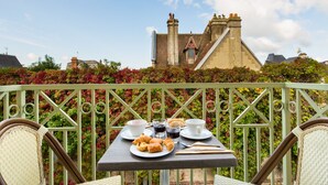 A table set with croissants, coffee, and a glass of water on a balcony with a view of a historic building. -  La Closerie – SPA & Résidence Hôtel (Deauville)