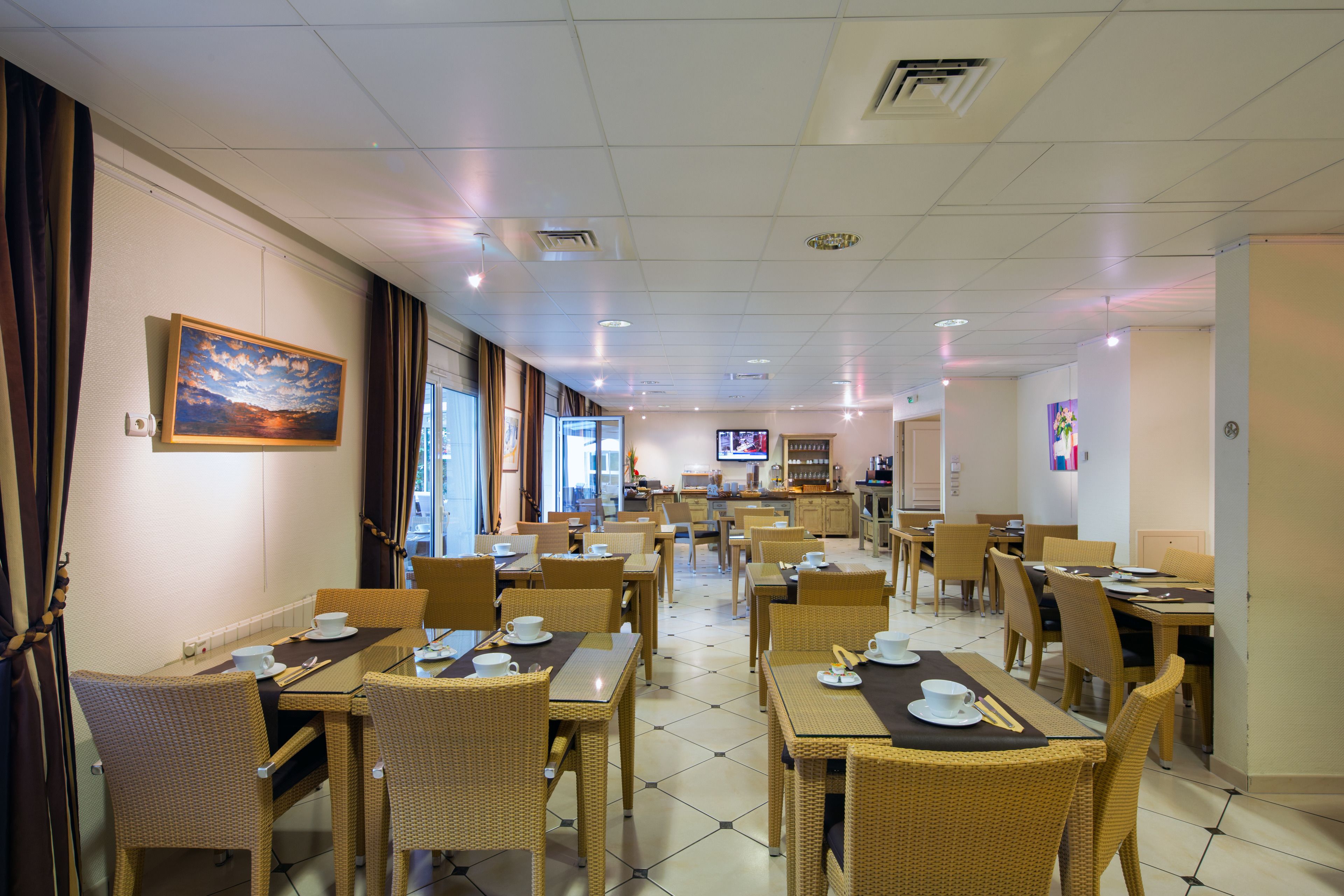 A hotel dining area with multiple tables and chairs, a television in the background, and a painting on the wall.