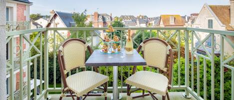 Un balcón con dos sillones de mimbre y una mesa dispuesta para una comida, con vistas a una zona residencial.